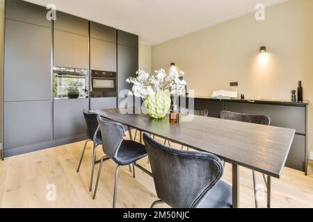 un tavolo da pranzo e sedie in una stanza con una cucina aperta sul lato opposto, c'è un vaso di fiori bianchi Foto Stock