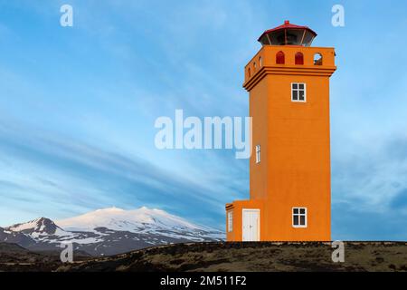 Faro di Svörtuloft, vista del faro con una montagna innevata sullo sfondo, regione occidentale, Islanda Foto Stock