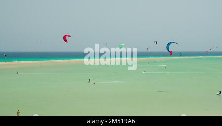 Kiters e surfisti tagliano le onde dell'oceano Atlantico sulla costa delle Isole Canarie. Sport estremi a Playa de Sotavento de Jandia, Fuerteventura Foto Stock