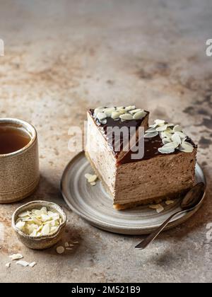 Due fette di cheesecake al cioccolato con petali di mandorla, tazza da tè su sfondo marrone. Spazio di testo, menu. Orientamento verticale Foto Stock