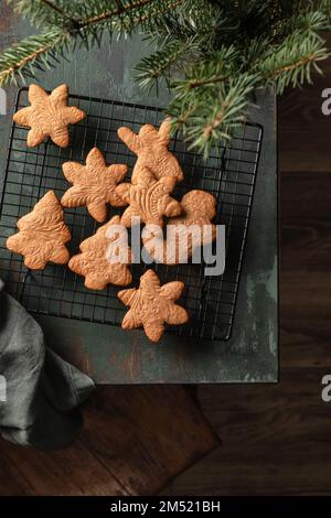 Biscotti di Natale o pani di zenzero di varie forme sulla griglia di raffreddamento della pasticceria sul tavolo di legno verde. Natale o composizione di nuovo anno con albero di natale, a. Foto Stock