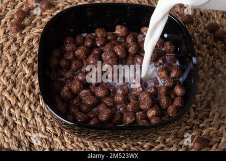 foto cioccolato colazione palline di cereali galleggianti nel latte e versando il latte sopra Foto Stock