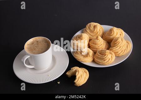 foto di una tazza bianca di caffè e di una torta di meringa su sfondo nero Foto Stock