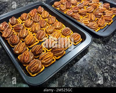 Caramelle al cioccolato fuso e caramello con noci pecan su pretzel morso su teglie Foto Stock