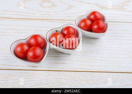 Tomatos tomatos di ciliegio rosso maturo in ciotola a forma di cuore Foto Stock