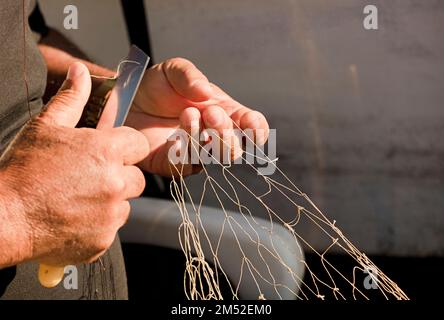 mani di pescatore con reti e coltello per la riparazione Foto Stock