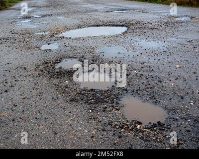 Pothole su una strada asfaltata in una giornata invernale piovosa. Concetto di rischio e problemi di traffico Foto Stock