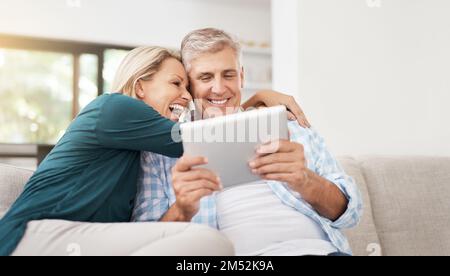 Questo è semplicemente il meglio. una coppia matura affettuosa che usa un tablet mentre si siede sul divano a casa. Foto Stock