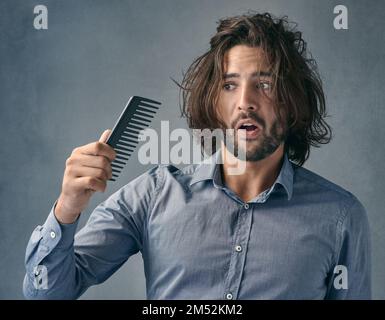 Arent supponete di riparare il pasticcio sulla mia testa. un bel giovane che guarda il pettine dopo aver pettinato i capelli. Foto Stock