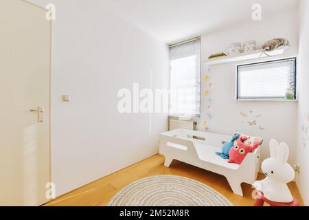 camera per bambini con pareti bianche e pavimento in legno, decorata con tonalità rosa, blu e verde Foto Stock