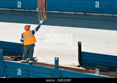 Infilare il casco e il giubbotto scarica tubi metallici e raccordi dalla carrozzeria del camion in una giornata limpida. Background di produzione. Flusso di lavoro autentico in cantiere. Slinger al lavoro.. Foto Stock