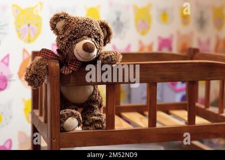 un morbido orsetto di orsacchiotto marrone si siede in un letto di legno per bambini in una stanza per bambini su uno sfondo sfocato Foto Stock