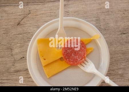 affettato formaggio e salsiccia su un piatto di plastica con una forchetta sul tavolo Foto Stock