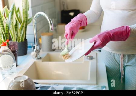 Mani femminili in guanti rosa lavando piatti con spazzola primo piano Foto Stock