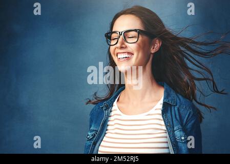 Non potete battere quella sensazione di aria fresca. Studio shot di una giovane donna con aria soffiata in faccia su uno sfondo blu. Foto Stock