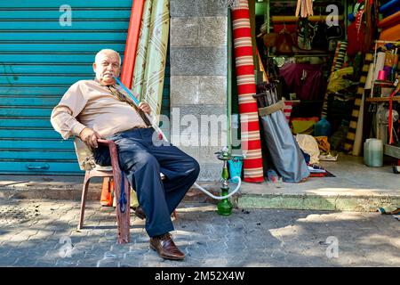 Amman Giordania. Un cittadino anziano rilassato che fuma narghilè vicino al suo negozio Foto Stock