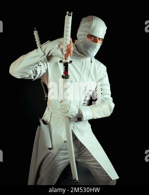 Ninja posa per una foto su uno sfondo nero, un ninja maschio in un kimono bianco. Il combattente esercita una spada affilata Foto Stock