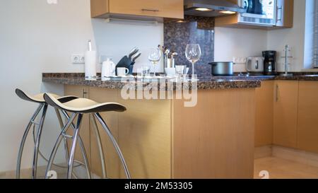 Mobili da cucina con sgabelli per sedersi a mangiare e vari utensili da cucina sopra il piano della cucina. Foto Stock