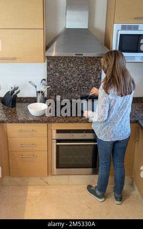 Donna bianca anziana che cucina con una pentola e vari utensili da cucina intorno a lei. Foto Stock