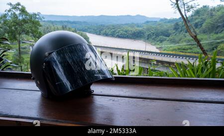 Casco da motocicletta sul tavolo con splendide viste di ponti e fiumi sullo sfondo di alberi verdi, colline ondulate e montagne Foto Stock