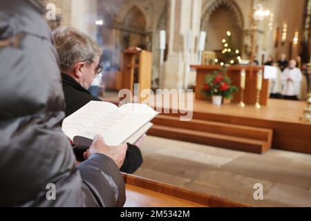 Erfurt, Germania. 25th Dec, 2022. Un partecipante con un libro di inni si siede durante il servizio alla Messa Pontificia nella solennità della Natività del Signore in S. Cattedrale di Maria. Credit: Bodo Schackow/dpa/Alamy Live News Foto Stock