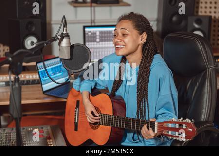 Donna multirazziale, cantante musicista compositore chitarrista e songwriter che provano la nuova traccia in studio di registrazione del suono Foto Stock