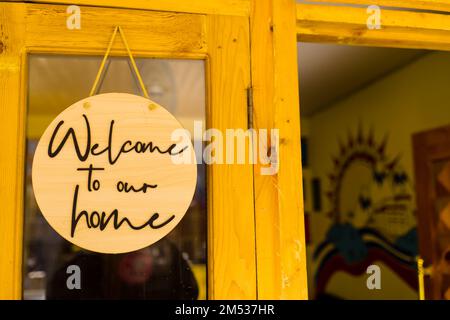 Un primo piano di un cartello di legno rotondo che dice "Benvenuti a casa nostra" di fronte alla porta di una casa Foto Stock