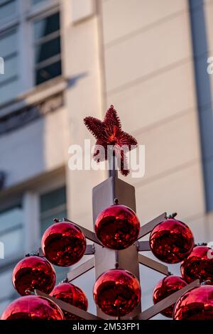 una stella rossa sulla cima di palline rosse di natale di fronte a un edificio sfocato Foto Stock