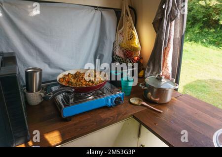 Tipica situazione di Vanlife durante la cena in cucina con padella su una stufa a gas Foto Stock