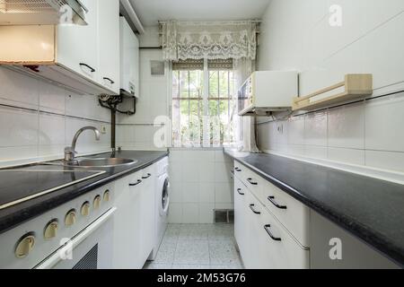 cucina stretta con armadi su entrambi i lati della parete con armadi bianchi e ripiani grigi Foto Stock