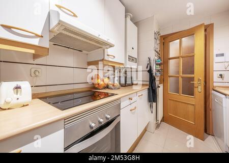 cucina con armadi in legno bianco con elettrodomestici bianchi da incasso, scaldabagno a gas naturale e ripiano in legno Foto Stock