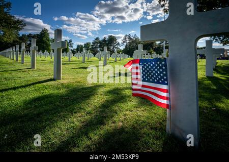 Una bandiera americana in piedi presso la lapide di un soldato ucciso al cimitero di guerra in Normandia Foto Stock