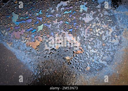 Macchie di olio o benzina sono sparse casualmente sull'asfalto dopo la pioggia. Primo piano di sfondo astratto Foto Stock