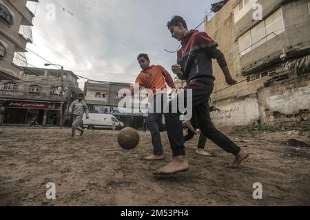 Striscia di Gaza. 25th Dec, 2022. I bambini rifugiati palestinesi giocano a calcio nelle strade del campo di Jabalia durante una giornata di pioggia nella striscia di Gaza settentrionale. A causa degli elevati tassi di disoccupazione e della mancanza di opportunità di lavoro a Gaza, un numero crescente di famiglie si trova ad affrontare la povertà dopo aver perso il lavoro durante il blocco di Gaza e le guerre israeliane contro la striscia di Gaza. (Credit Image: © Mahmoud Issa/Quds Net News via ZUMA Press Wire) Credit: ZUMA Press, Inc./Alamy Live News Foto Stock