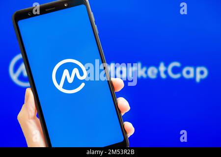 Ucraina, Odessa - Ottobre, 9 2021: Tenere la mano mobile con l'app CoinMarketCap in esecuzione sullo schermo dello smartphone con il logo CMC sullo sfondo. L'autorità per i dati di criptovaluta più affidabile al mondo Foto Stock