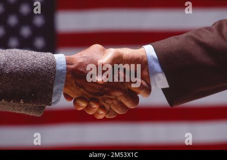Colpo simbolico agli uomini d'affari, scuotendo le mani con una bandiera americana sullo sfondo Foto Stock