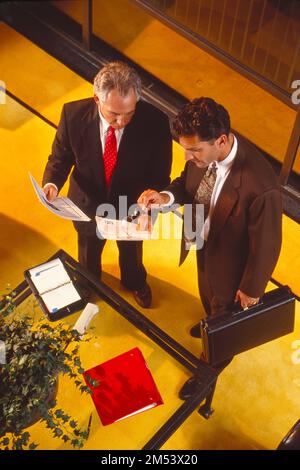 Guarda la vista in basso di due uomini d'affari che guardano i documenti tenendo una valigetta Foto Stock