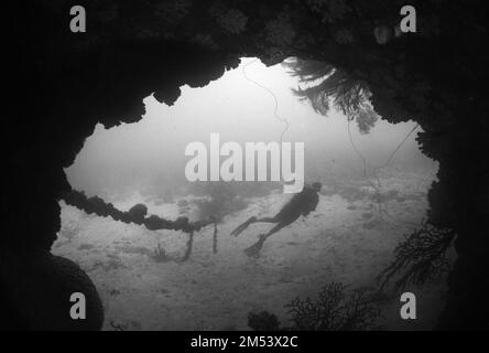 Una scala di grigi di un subacqueo in una muta catturata nuotando lontano da una grotta subacquea Foto Stock
