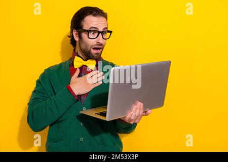 Foto del giovane uomo impressionato gentleman indossare ponticello verde con camicia bowtie touch petto scioccato guardare film laptop isolato su sfondo giallo Foto Stock