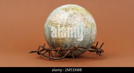 Il concetto di simbolismo. Su una superficie marrone si trova un globo, che è circondato da filo spinato. Banner. Foto Stock