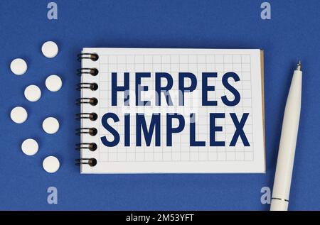 Concetto medico. Su uno sfondo blu, una penna, compresse e un blocco note con l'iscrizione - HERPES SIMPLEX Foto Stock