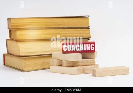 Concetto di istruzione. Su una superficie bianca, una pila di libri e blocchi di legno, su un blocco rosso c'è un'iscrizione - COACHING Foto Stock