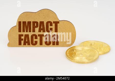 Concetto di business e tecnologia. Bitcoins giacciono su una superficie bianca e c'è un segno - una nuvola con l'iscrizione - FATTORE DI IMPATTO Foto Stock