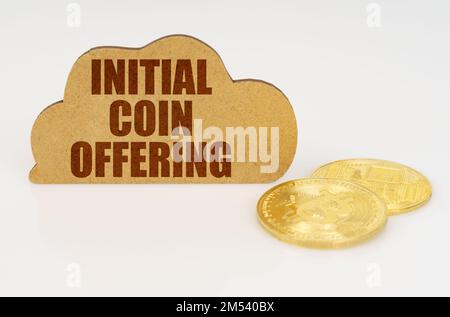 Concetto di business e tecnologia. Bitcoins giacciono su una superficie bianca e c'è un segno - una nuvola con l'iscrizione - offerta di moneta iniziale Foto Stock