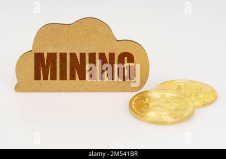 Concetto di business e tecnologia. Bitcoins giacciono su una superficie bianca e c'è un segno - una nuvola con l'iscrizione - Mining Foto Stock