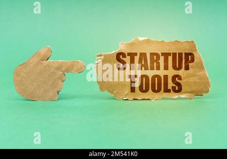 Concetto di business e tecnologia. Su una superficie verde, una mano di cartone punta a un cartello con la scritta Startup Tools Foto Stock