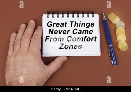 Concetto aziendale. Su una superficie marrone ci sono monete, una penna e un blocco note con l'iscrizione - grandi cose non sono mai venuto da Comfort zone. Il notebook è Foto Stock