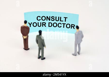 Concetto medico. Figure in miniatura di persone in piedi di fronte a un segno blu con l'iscrizione - consultare il medico Foto Stock