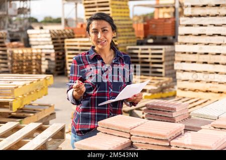 Il responsabile della donna tiene i registri dei materiali da costruzione nell'area aperta del deposito di costruzione Foto Stock