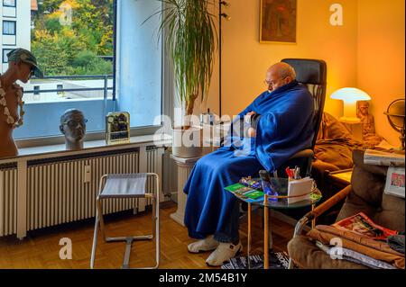 Vecchio avvolto in coperte, risparmiare energia, congelare a causa di Putin, risparmiare costi di riscaldamento, bassa temperatura ambiente, Baviera, Germania Foto Stock